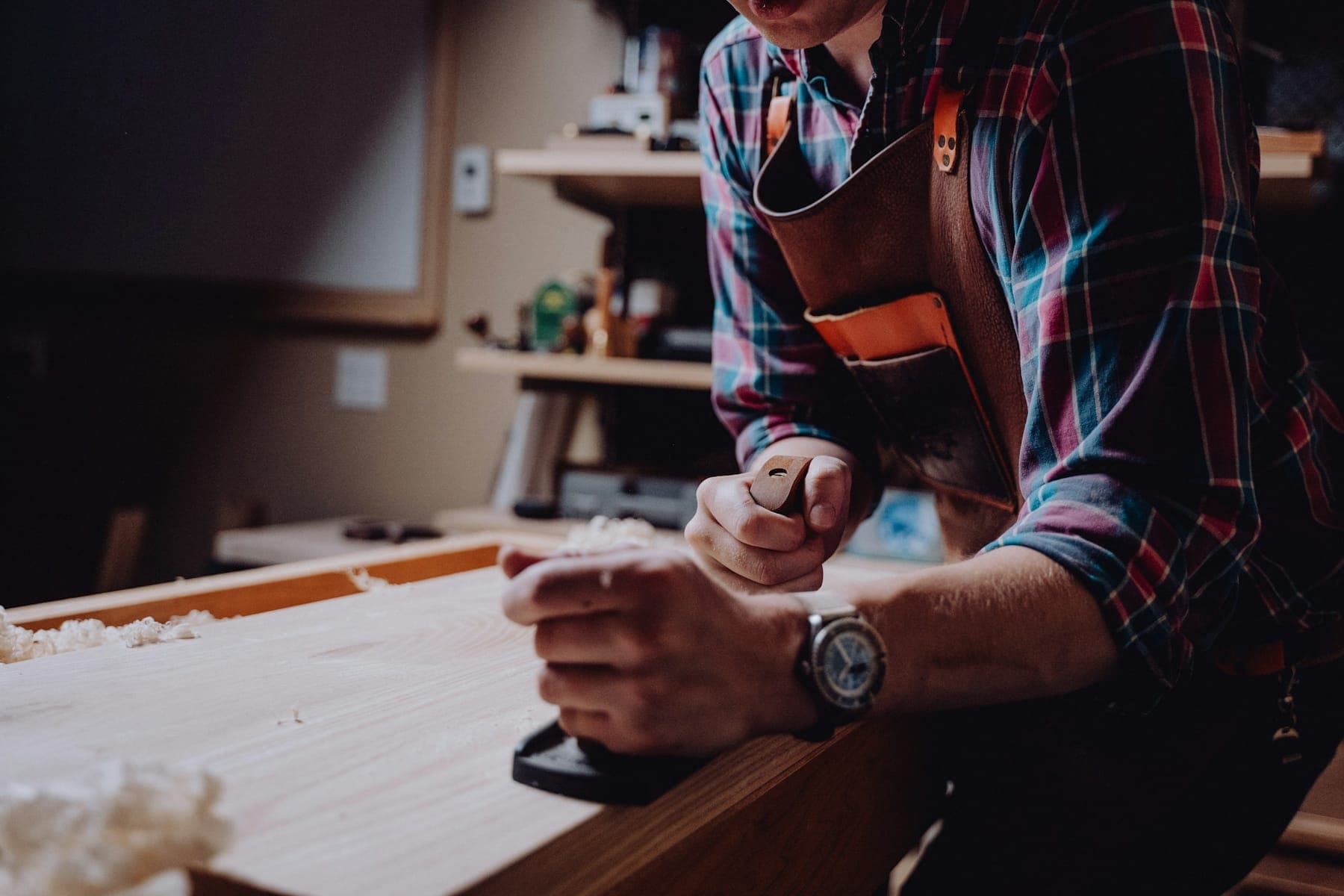 Hands guiding a wood plane across a board in a workshop