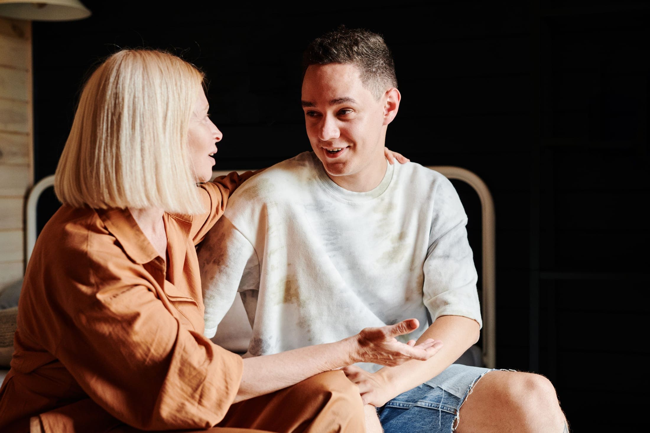 A woman and a young man sitting side by side in conversation, leaning in as he talks and she listens