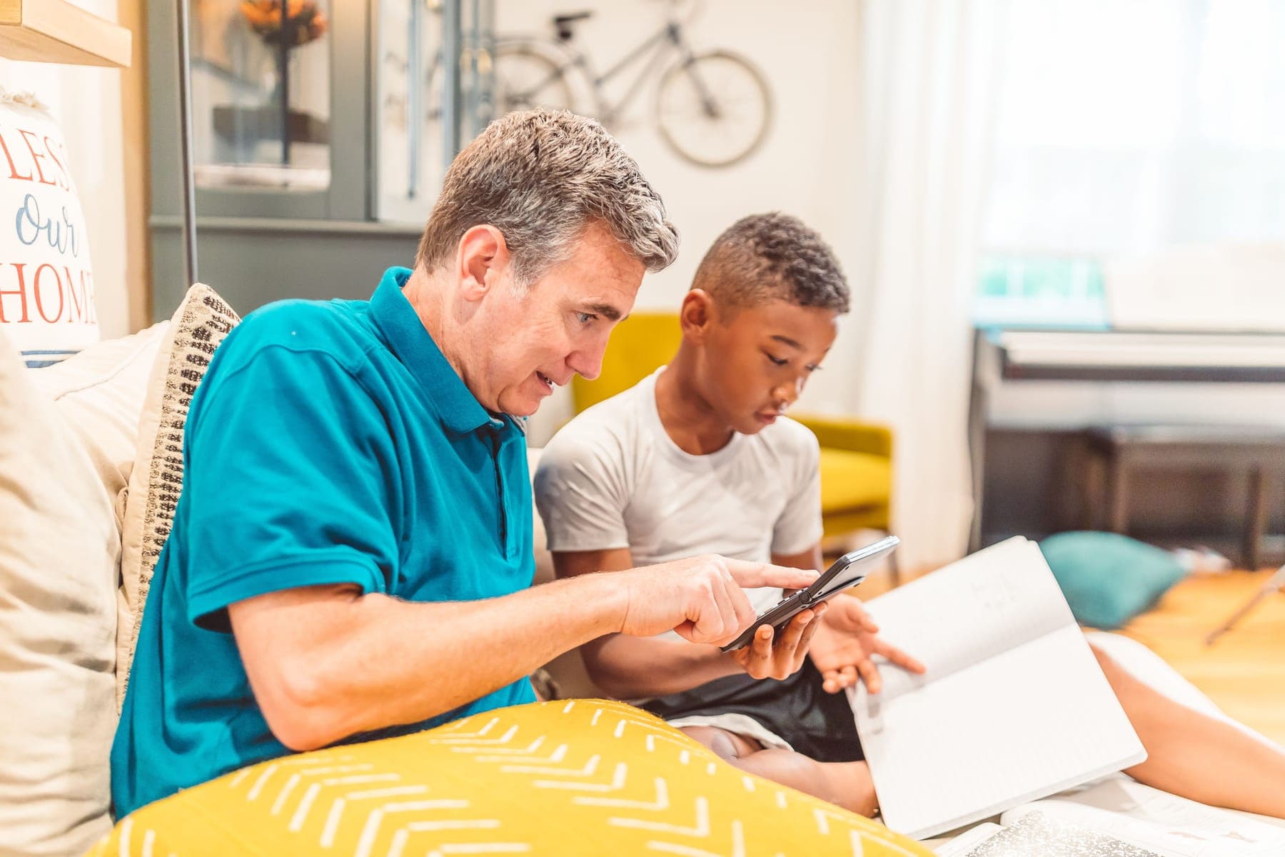 An older man and a young boy sitting together on a sofa, working through a book side by side