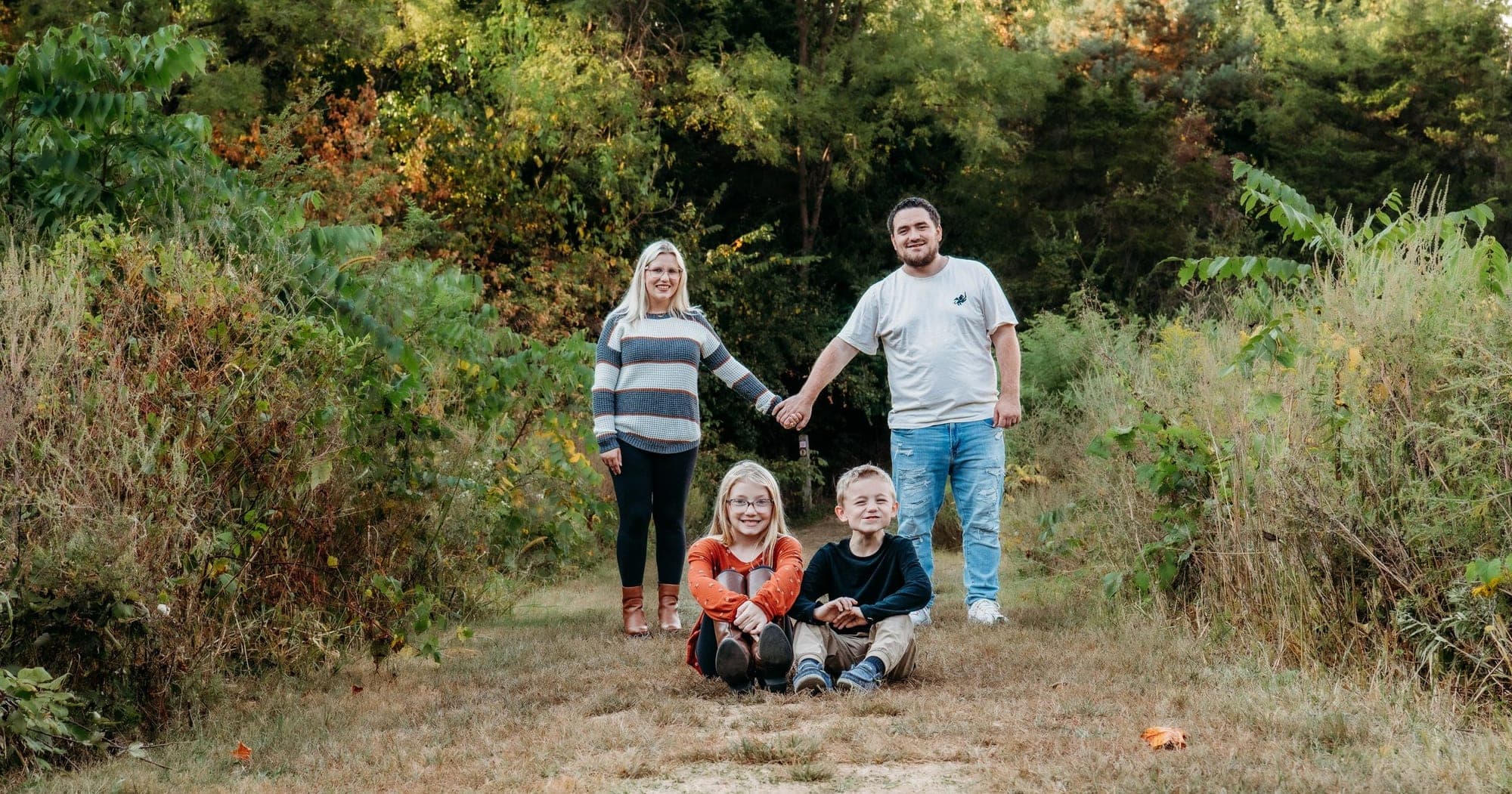 A family of four together on a wooded trail in early autumn