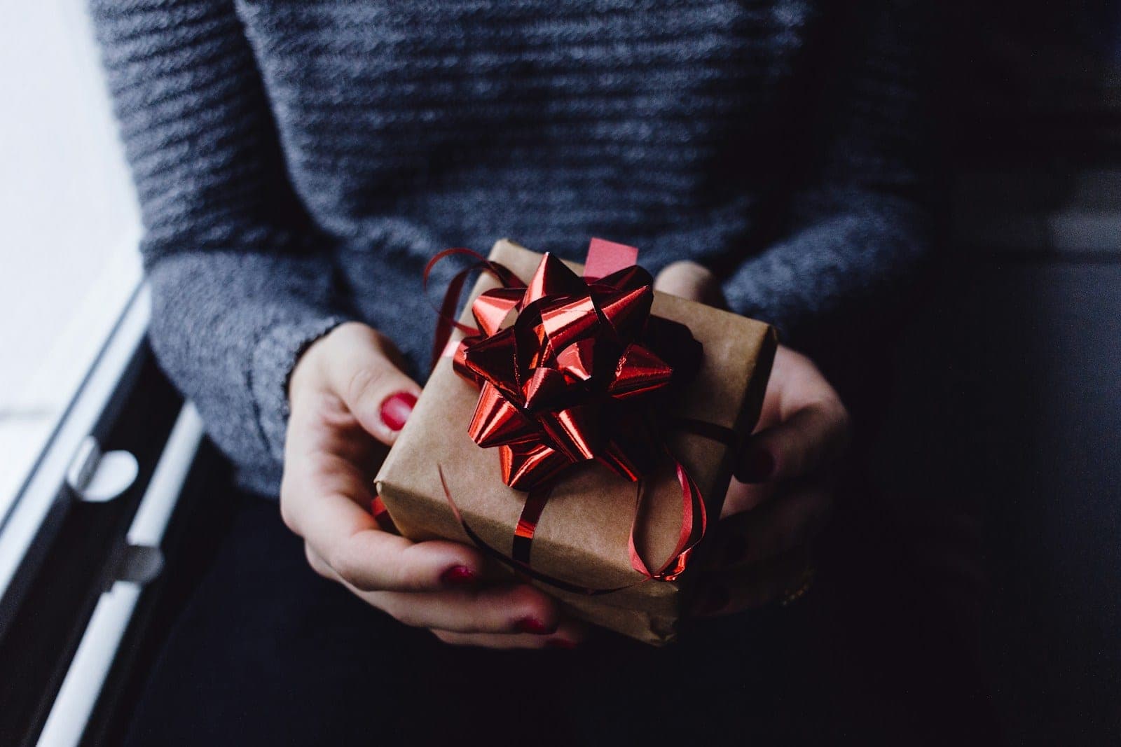 Hands holding a Christmas gift wrapped in brown paper with a red bow